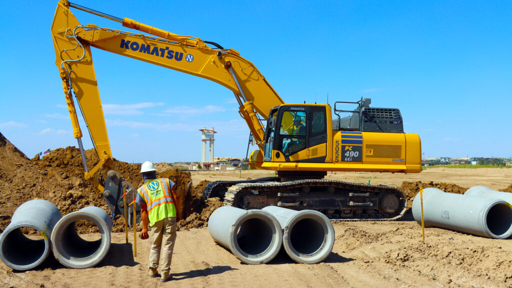 Excavator moving cement pipes on job site